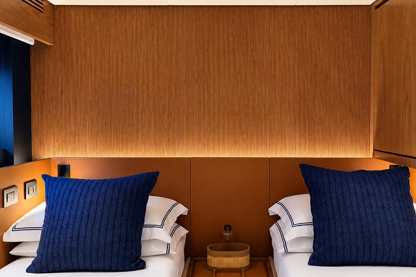 Bed with navy knitted cushions, white linen and an oak headboard panel