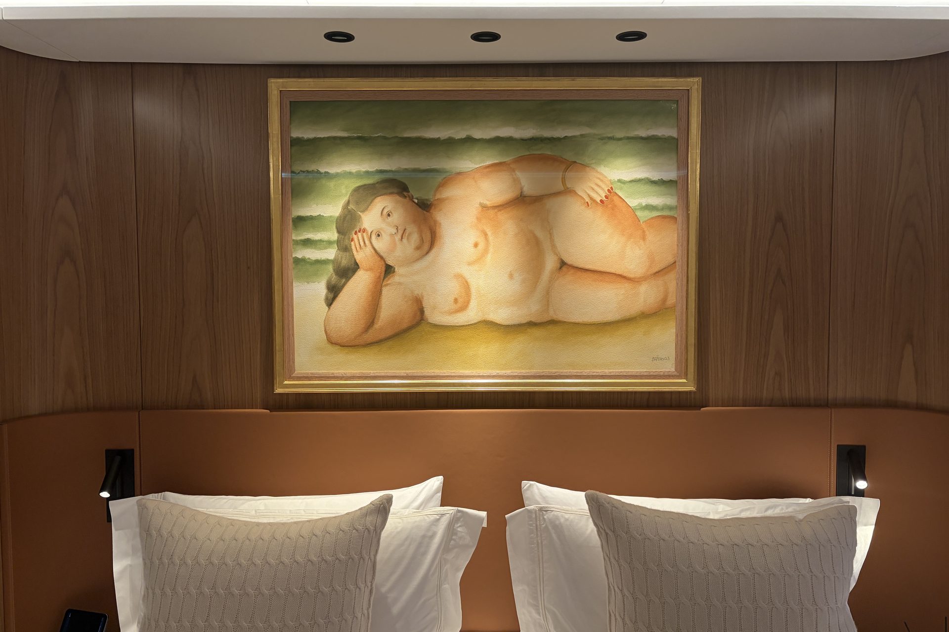 Master cabin headboard in tan leather and oak, with a large framed painting above the pillows