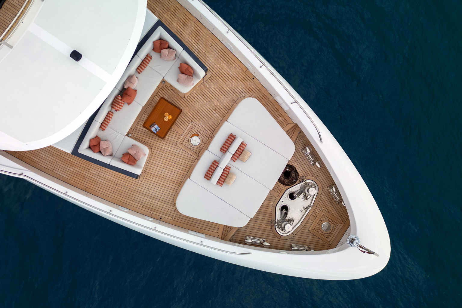 Aerial view of the motor yacht's foredeck: teak deck, white sun pads and a lounge with terracotta cushions