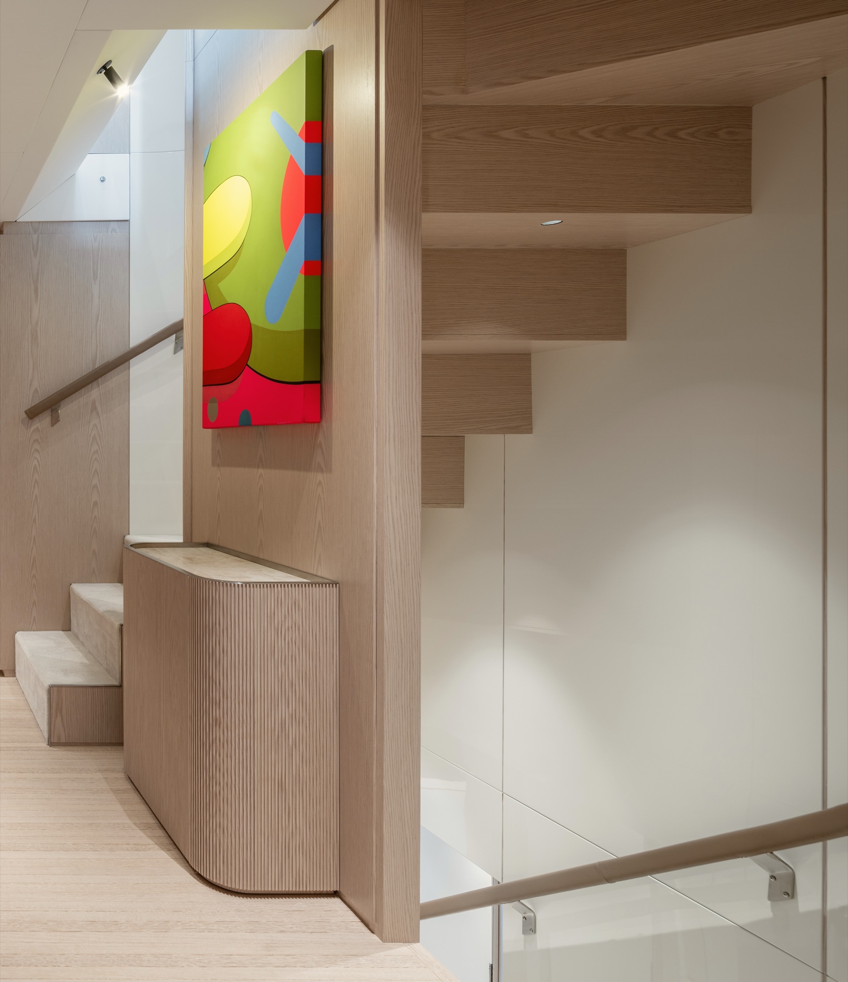 Staircase in pale oak with a colourful artwork and a fluted cabinet at its foot
