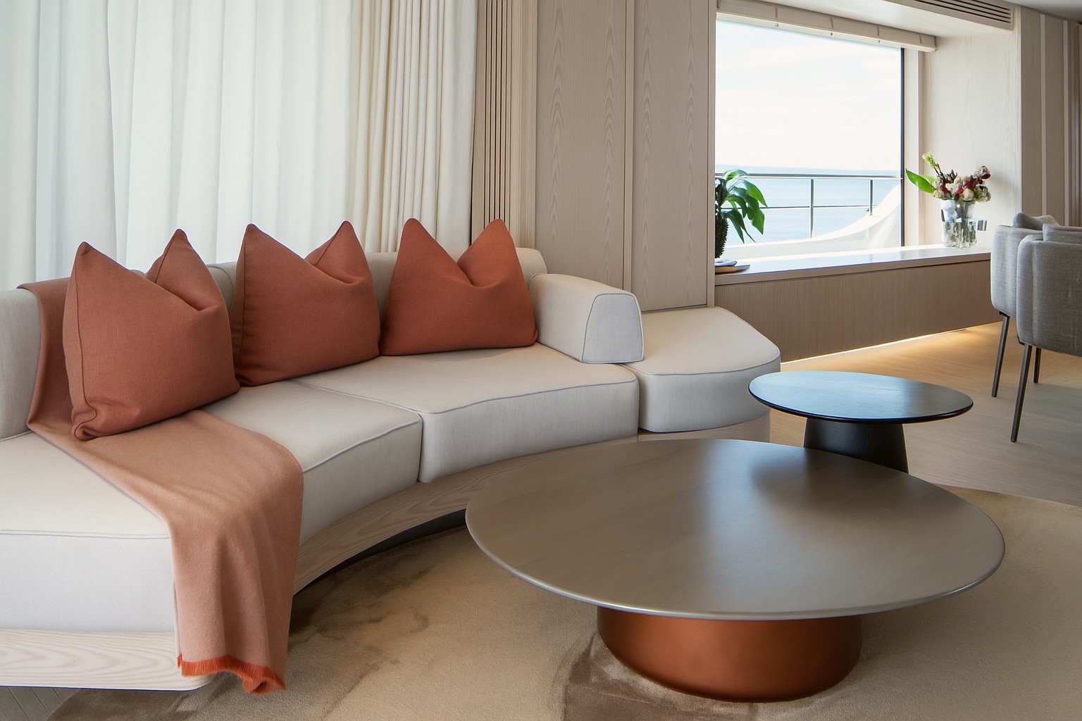 Main salon with a curved cream sofa, terracotta cushions and throw, and two round coffee tables facing the sea