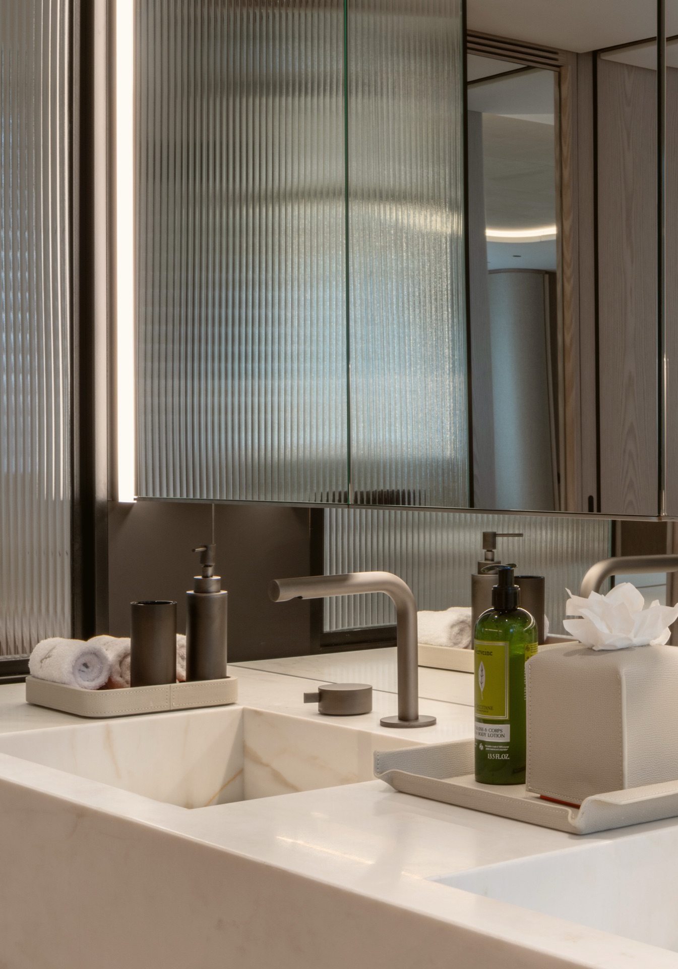 Bathroom vanity in veined marble with brushed-steel taps and fluted glass cabinet doors