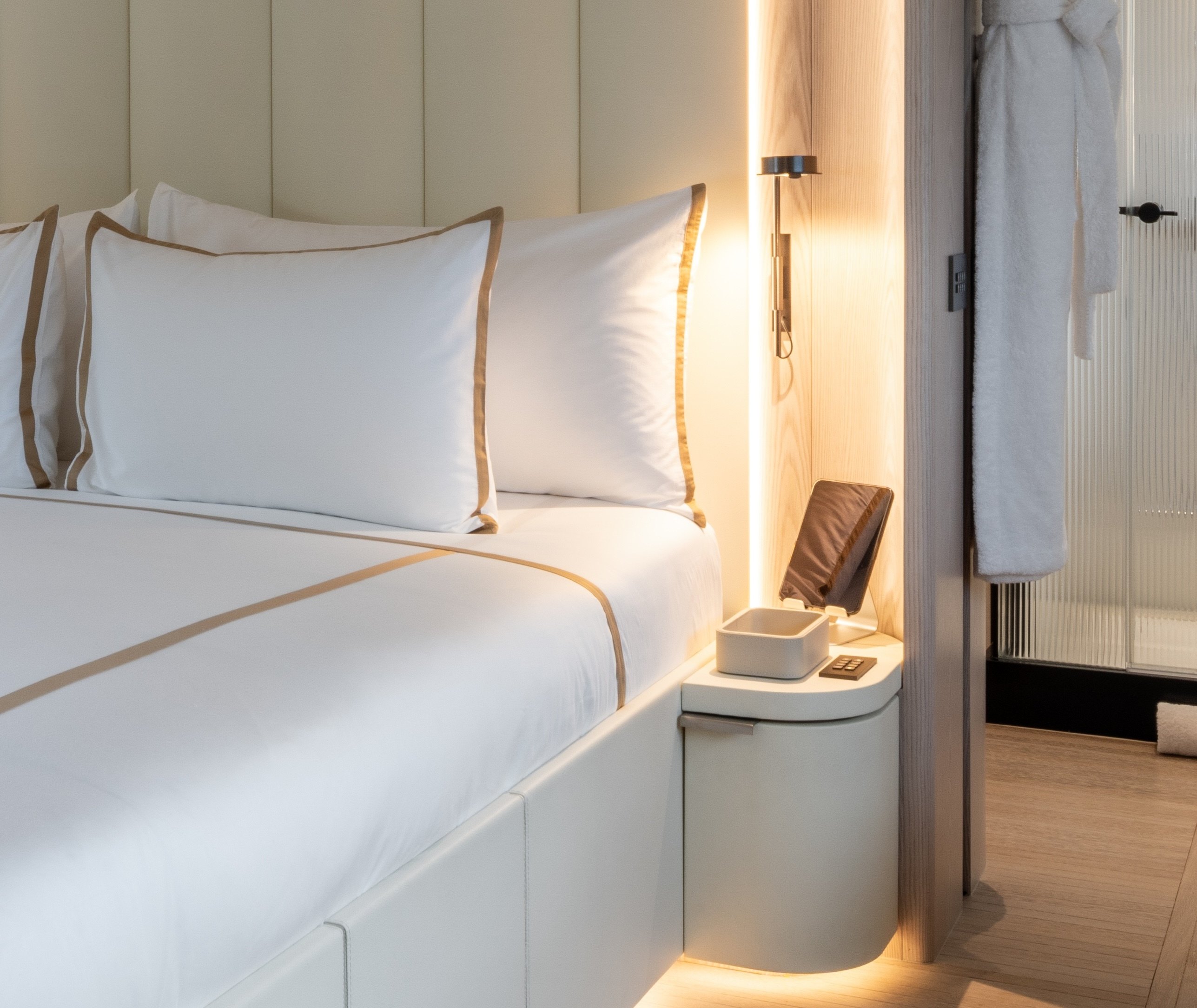 Bed with white linen trimmed in beige, upholstered headboard and a backlit nightstand