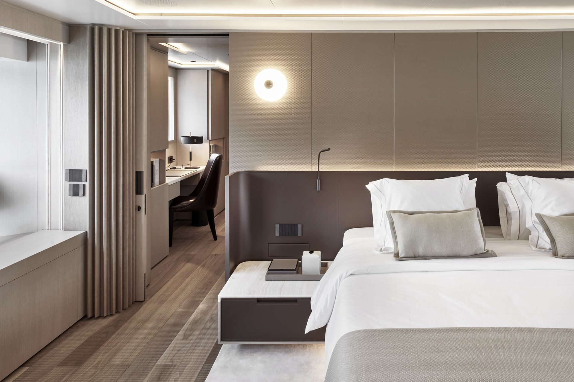 Master cabin in pale oak with a desk, a curved leather headboard wall and a round wall light