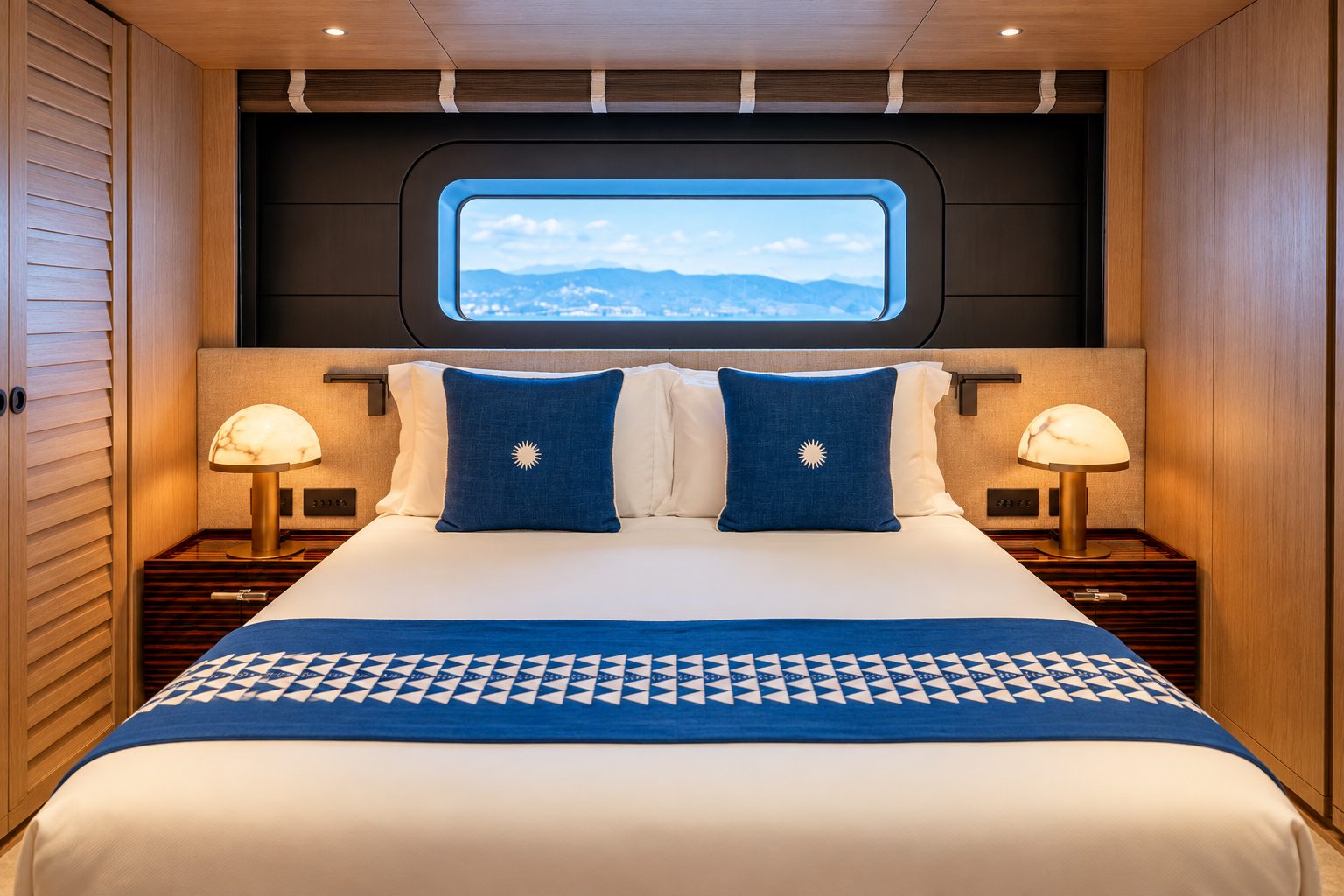 Guest cabin with a wide window above the bed, navy cushions, a blue runner and brass bedside lamps