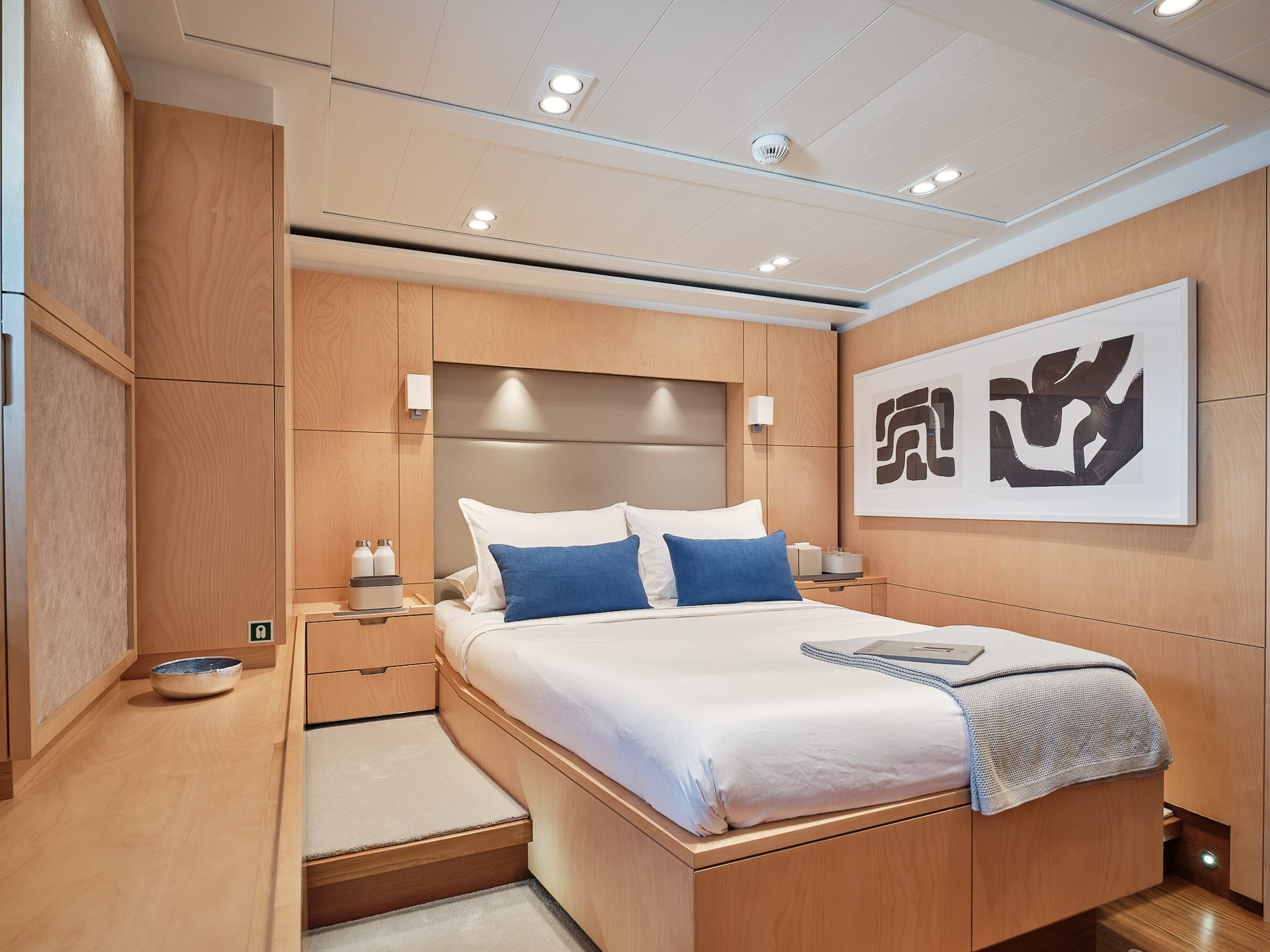 Master cabin in birch with blue cushions, framed artworks and a bedside lamp